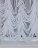 A close-up view of a white ruffled curtain hanging in front of a window. Produktbild-Vorschau