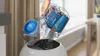 A hand is emptying a vacuum cleaner dustbin into a trash can. Produktbild-Vorschau
