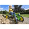 A young boy is riding a green pedal tractor in an outdoor setting with a pile of dirt and trees in the background. Podgląd zdjęcia produktu