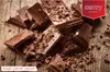 A pile of chocolate pieces sprinkled with chocolate shavings on a wooden surface. Podgląd zdjęcia produktu
