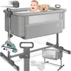 A baby in a crib with a teddy bear, surrounded by product accessories and features. Produktbild-Vorschau