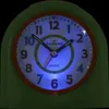 A close-up of a green and orange analog alarm clock with blue backlighting. Produktbild-Vorschau