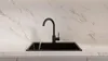 A black kitchen faucet with water running into a black sink, set against a marble-patterned backsplash and countertop. Produktbild-Vorschau
