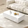 A modern living room scene with a white coffee table in the foreground and a beige sectional sofa in the background. Produktbild-Vorschau