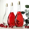 Three glass bottles with cork stoppers, two filled with red liquid and one empty, sit on a wooden surface with raspberries scattered around. A sprig of eucalyptus is in the background. Voir les images du produit