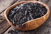 A wooden bowl filled with wild rice on a wooden surface. Produktbild-Vorschau