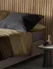 A bed with pillows and a blanket, next to a small side table with decorative items. Produktbild-Vorschau