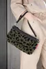 A person holding a small leopard-print pouch bag. Produktbild-Vorschau