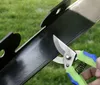 A close-up of garden shears cutting a black metal edge, with green grass in the background. Podgląd zdjęcia produktu