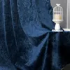 A close-up of a dark blue curtain with a floral pattern, draped over a surface. A white candle holder with a candle is visible on the right. Produktbild-Vorschau