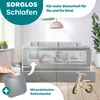 A baby sleeping in a bed with a safety rail, a hand holding a baby bottle, and a toy wooden bike. Produktbild-Vorschau