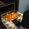 A person is taking a glass baking dish filled with roasted carrots out of an oven. Podgląd zdjęcia produktu