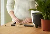 A person's hands are shown assembling or preparing a plant watering system on a wooden table. Produktbild-Vorschau