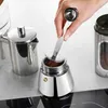 A person's hand is shown using a scoop to add coffee grounds to a stovetop espresso maker. Voir les images du produit
