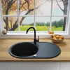 A black granite kitchen sink with a faucet is shown on a wooden countertop, with a large window in the background overlooking a scenic autumn landscape. Produktbild-Vorschau