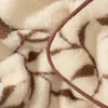 A close-up view of a fluffy blanket with a brown pattern and a brown trim. Produktbild-Vorschau