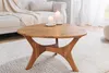 A wooden coffee table with two lit candles on it, placed on a fluffy white rug in a living room setting with a sofa in the background. Produktbild-Vorschau