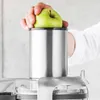 A hand is holding a green apple over the top of a stainless steel juicer. Náhľad obrázku produktu