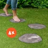 A person's bare feet walking on a grassy lawn, stepping on round, wood-like stepping stones. Anteprima dell’immagine prodotto