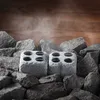 Two stone blocks with holes are surrounded by sauna rocks, with steam rising in the background. Produktbild-Vorschau