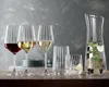 A collection of glassware, including wine glasses and a pitcher, arranged on a wooden surface against a textured gray background. Náhled obrázku produktu