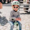 A young child wearing a helmet and sunglasses is sitting on a mint green scooter. Podgląd zdjęcia produktu