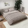 A bedroom scene with a bed dressed in plaid bedding, a large plant, and framed artwork. Náhľad obrázku produktu