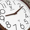 Close-up view of a modern wall clock with a white face, brown hands, and black numbers. Voir les images du produit