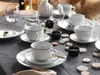 A table setting with white porcelain cups and saucers, small black bowls, and decorative wooden slices. Náhľad obrázku produktu