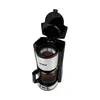 A black and silver Tesla coffee maker with the lid open, showing the filter basket with coffee grounds and the glass carafe filled with coffee. Produktbild-Vorschau