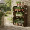 A rustic wooden crate shelving unit filled with various potted plants, placed against a brick wall in a garden setting. Anteprima dell’immagine prodotto