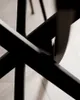 A close-up abstract shot of the black metal legs of a round table, intersecting in a geometric pattern. Produktbild-Vorschau