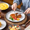 A person is eating a meal from a set of stoneware dishes on a wooden table. Produktbild-Vorschau