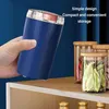 A hand holding a blue electric grinder above a shelf with glass jars. Produktbild-Vorschau