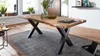 A dining table with a live edge wooden top and black X-shaped legs, placed on a rug in a well-lit room. Produktbild-Vorschau