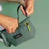 A person's hands are shown attaching a strap to a green Pacsafe bag. Produktbild-Vorschau