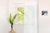 A white curtain rail mounted above a window, with a sheer white curtain partially drawn. Produktbild-Vorschau