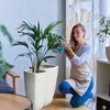 A woman is watering a plant in a modern living room setting. Náhľad obrázku produktu