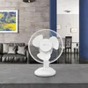 A white table fan is displayed on a gray surface in a living room setting. Náhľad obrázku produktu