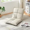 A beige floor chair is placed on a rug in a room with a plant and a cabinet in the background. Voir les images du produit