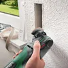 A person is using an oscillating multi-tool to cut a rectangular opening in a textured wall, next to a window frame. Voir les images du produit