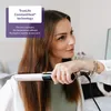 A woman is using a hair straightener on her hair. Produktbild-Vorschau
