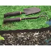 Gardening tools are placed on grass next to a garden bed with mulch. Náhled obrázku produktu