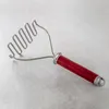 A potato masher with a red handle is shown on a gray surface. Produktbild-Vorschau