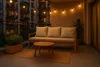 A cozy balcony at dusk, furnished with a sofa, coffee table, and plants, illuminated by string lights. Produktbild-Vorschau