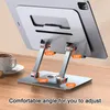 A silver tablet stand is shown on a wooden desk, with a cup of coffee in the background. The stand is adjustable and features indicators showing 180-degree rotation. Produktbild-Vorschau