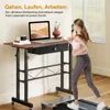 A woman is jogging on a treadmill next to a height-adjustable desk with a laptop on it. Anteprima dell’immagine prodotto