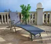 A gray chaise lounge chair is placed on a tiled patio next to a decorative plant and a white sphere on a pedestal, with a railing and sky in the background. Produktbild-Vorschau
