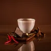 A cup of hot chocolate with chocolate pieces, chili peppers, and cinnamon sticks. Produktbild-Vorschau