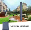 A garden scene with a tall, grey cover for a clothes dryer standing upright. A smaller grey pouch is in the foreground. Produktbild-Vorschau
